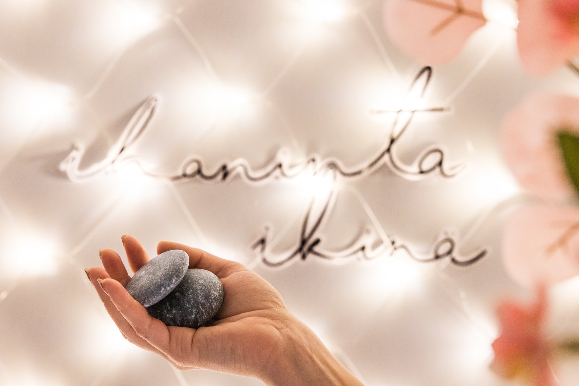 Geneesi energiahoidot. Ihmisen kädessä pyöreitä kiviä, taustan seinällä valoisa teksti "Ihaninta ikinä". | Business Joensuu, yrityspalvelut